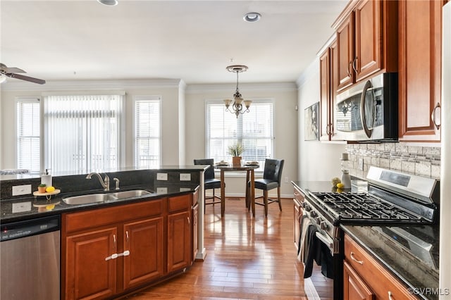 kitchen with hardwood / wood-style floors, appliances with stainless steel finishes, sink, dark stone countertops, and pendant lighting