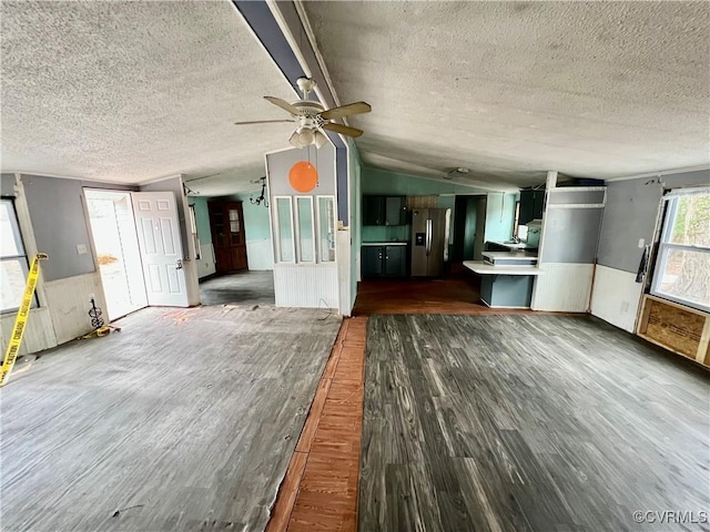 unfurnished living room featuring vaulted ceiling, dark wood-type flooring, a textured ceiling, and ceiling fan