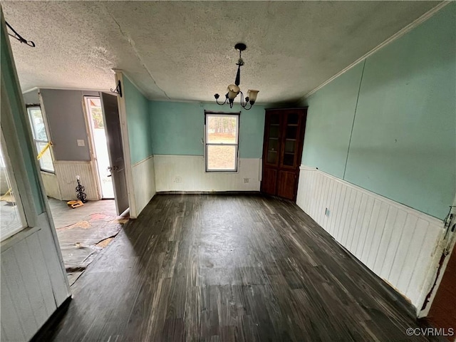 unfurnished dining area with dark wood-type flooring, an inviting chandelier, a textured ceiling, and ornamental molding