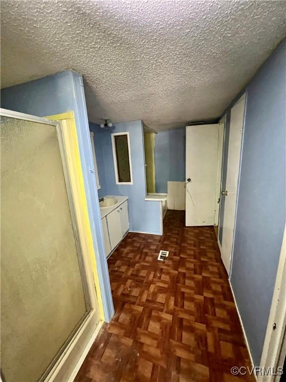 bathroom featuring walk in shower, vanity, parquet floors, and a textured ceiling