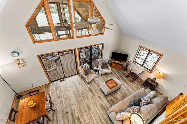 living room with ceiling fan, light hardwood / wood-style flooring, and a towering ceiling