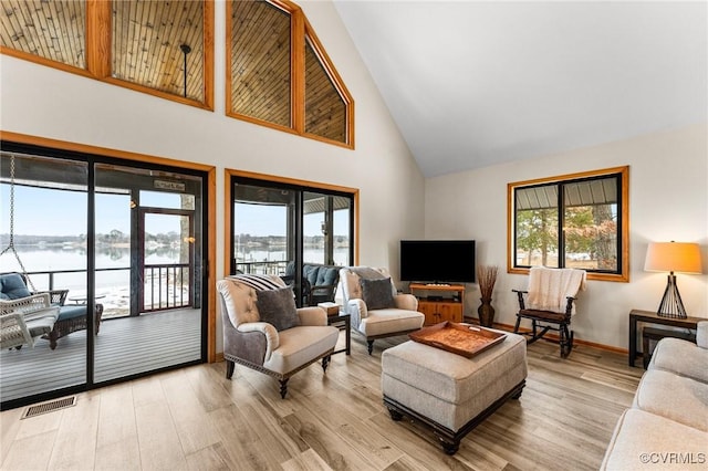 living room with light wood-type flooring, a water view, and a high ceiling