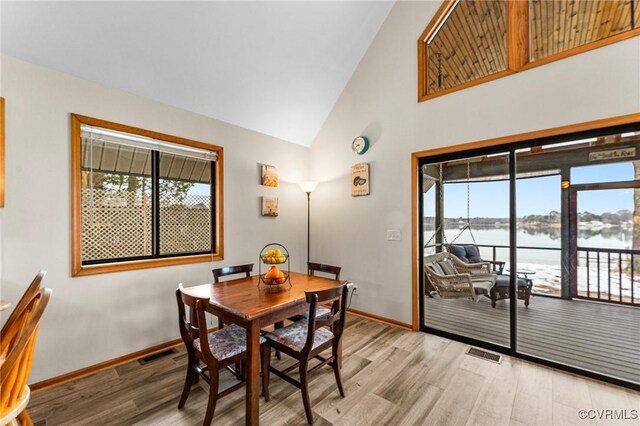 dining space with a water view, light hardwood / wood-style flooring, and high vaulted ceiling