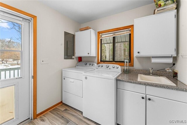 washroom with sink, light wood-type flooring, washing machine and dryer, electric panel, and cabinets