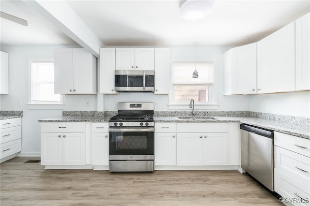 kitchen with sink, white cabinetry, light stone counters, decorative light fixtures, and appliances with stainless steel finishes