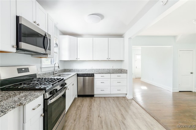 kitchen with white cabinetry, stainless steel appliances, sink, and light stone counters