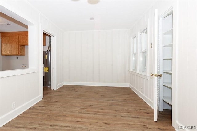 unfurnished dining area featuring water heater, ornamental molding, built in features, and wood-type flooring