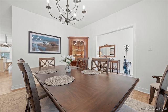 dining space with light wood-type flooring, a chandelier, and vaulted ceiling