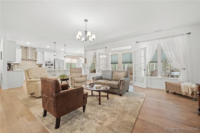 living room with light wood-type flooring, french doors, and a notable chandelier