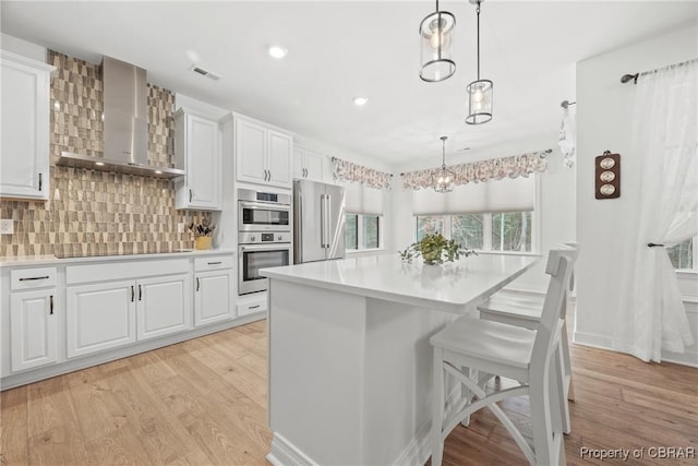 kitchen featuring decorative light fixtures, decorative backsplash, white cabinetry, appliances with stainless steel finishes, and wall chimney exhaust hood