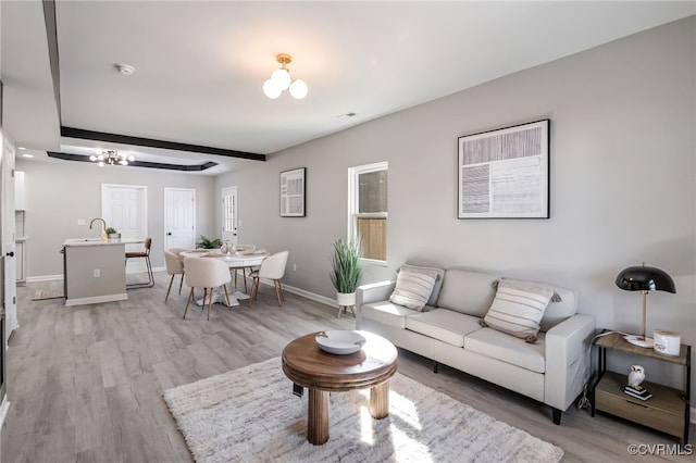 living room featuring beam ceiling, light wood-type flooring, a notable chandelier, and sink