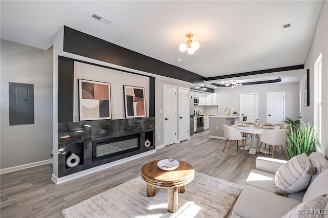 living room featuring light wood-type flooring, electric panel, sink, and a notable chandelier