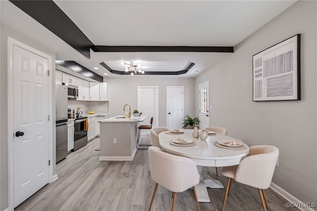 dining space with light hardwood / wood-style floors, a raised ceiling, and an inviting chandelier