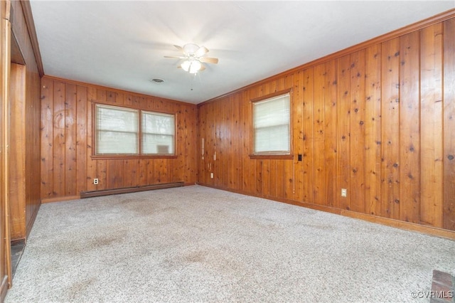 carpeted spare room with a baseboard radiator, ceiling fan, and wood walls