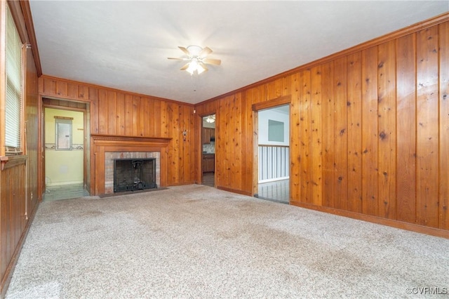 unfurnished living room with a tiled fireplace, crown molding, carpet flooring, and wood walls