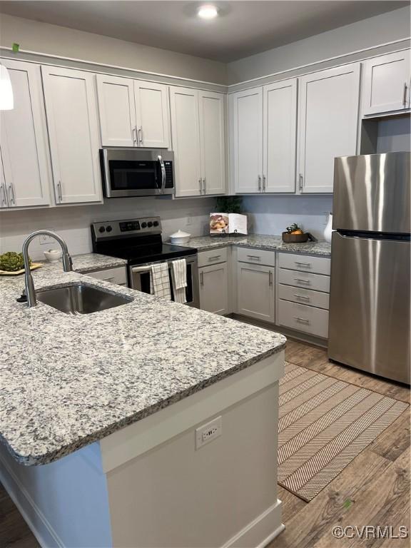 kitchen featuring appliances with stainless steel finishes, white cabinetry, sink, light wood-type flooring, and light stone counters