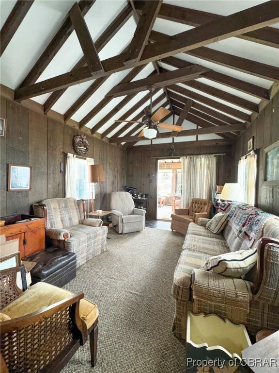 carpeted living room featuring ceiling fan, vaulted ceiling with beams, and wooden walls