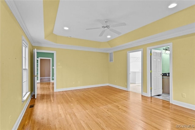 empty room with ceiling fan, wood-type flooring, a tray ceiling, and crown molding