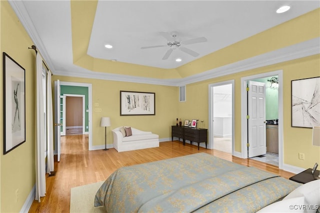 bedroom with ceiling fan, a raised ceiling, wood-type flooring, crown molding, and connected bathroom