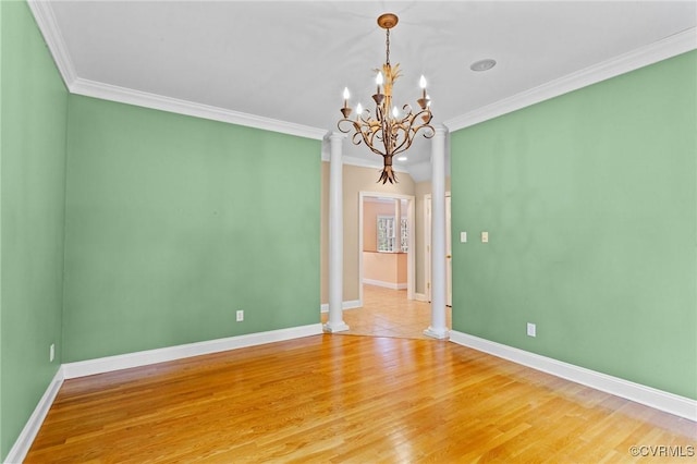 empty room with ornate columns, crown molding, wood-type flooring, and an inviting chandelier