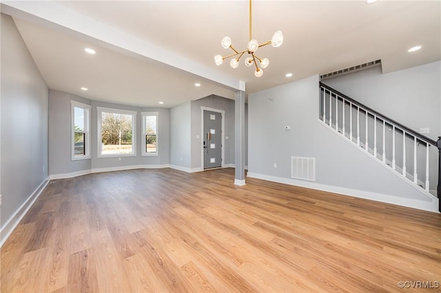 unfurnished living room featuring stairway, a chandelier, light wood finished floors, baseboards, and visible vents