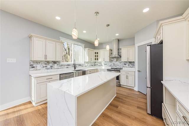 kitchen featuring a center island, decorative backsplash, wall chimney exhaust hood, appliances with stainless steel finishes, and light stone countertops