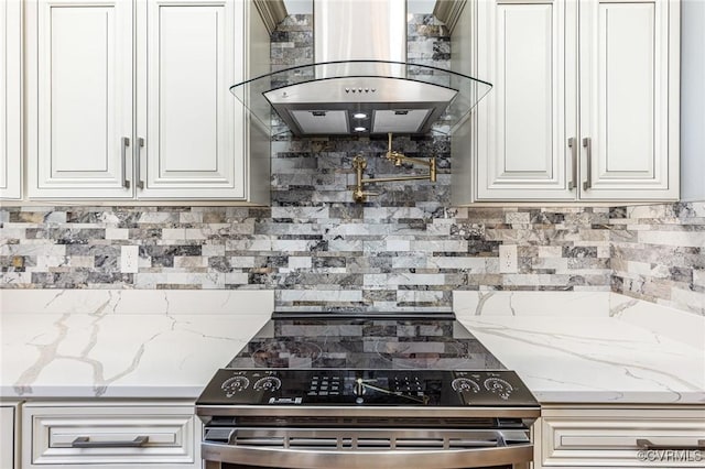 kitchen featuring light stone counters, tasteful backsplash, stainless steel electric range oven, wall chimney exhaust hood, and white cabinetry