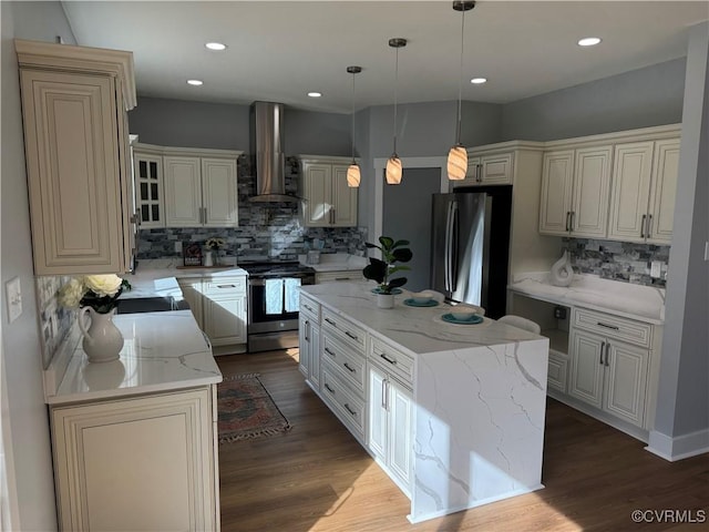 kitchen featuring a center island, tasteful backsplash, light stone counters, wall chimney range hood, and appliances with stainless steel finishes