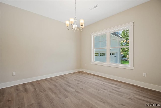 unfurnished room with an inviting chandelier, wood finished floors, visible vents, and baseboards