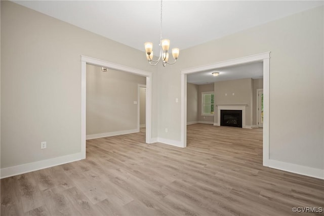 unfurnished living room with an inviting chandelier, light wood-style flooring, a fireplace, and baseboards