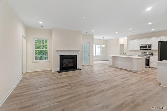 kitchen with stainless steel appliances, white cabinetry, open floor plan, light countertops, and an island with sink