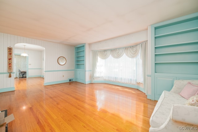 unfurnished living room featuring wood-type flooring and built in shelves