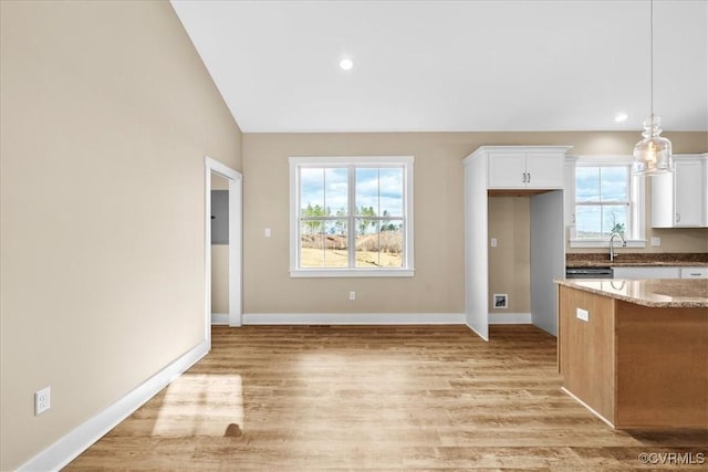 kitchen with hanging light fixtures, light stone countertops, white cabinetry, and light hardwood / wood-style floors