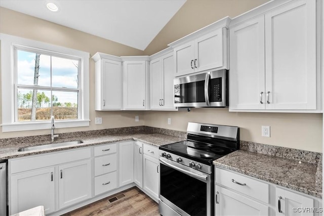 kitchen featuring white cabinetry, stainless steel appliances, light stone countertops, vaulted ceiling, and sink