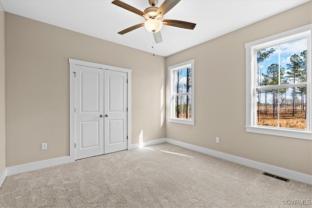 unfurnished bedroom featuring ceiling fan, a closet, light carpet, and multiple windows