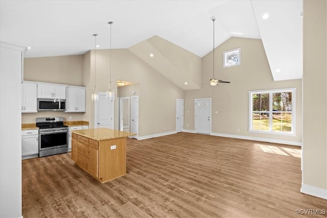 kitchen featuring a kitchen island, decorative light fixtures, white cabinetry, stainless steel appliances, and light stone counters