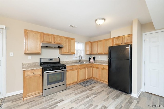 kitchen featuring black refrigerator, light brown cabinets, sink, stainless steel gas range oven, and light stone counters