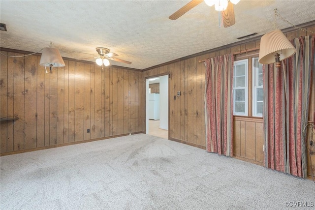 unfurnished room featuring wood walls, ornamental molding, ceiling fan, light carpet, and a textured ceiling