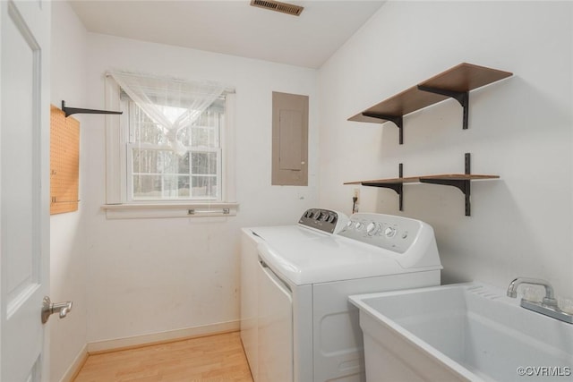 clothes washing area featuring independent washer and dryer, electric panel, light hardwood / wood-style floors, and sink