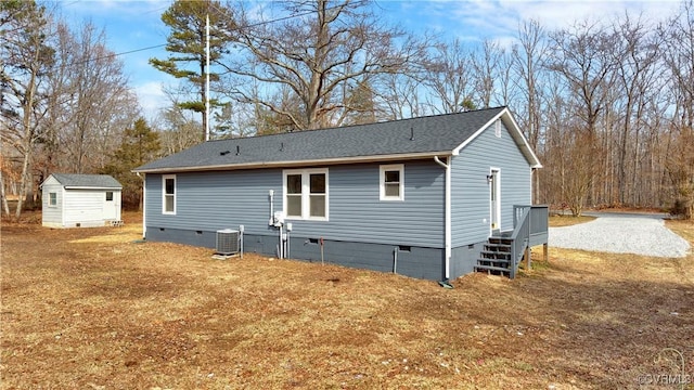 back of property with roof with shingles, crawl space, an outbuilding, a storage unit, and central air condition unit