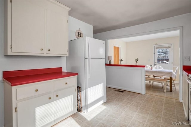 kitchen featuring white refrigerator, white cabinetry, and range