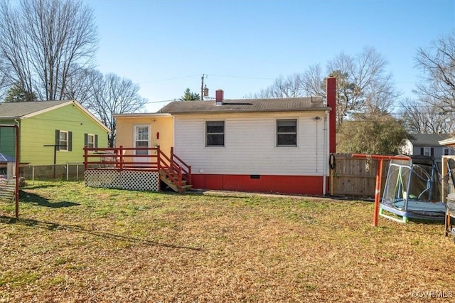 back of house with a trampoline, a deck, and a lawn