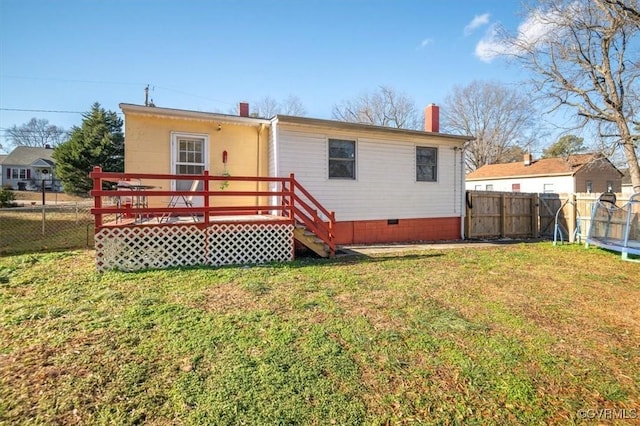 rear view of property featuring a deck, a trampoline, and a yard