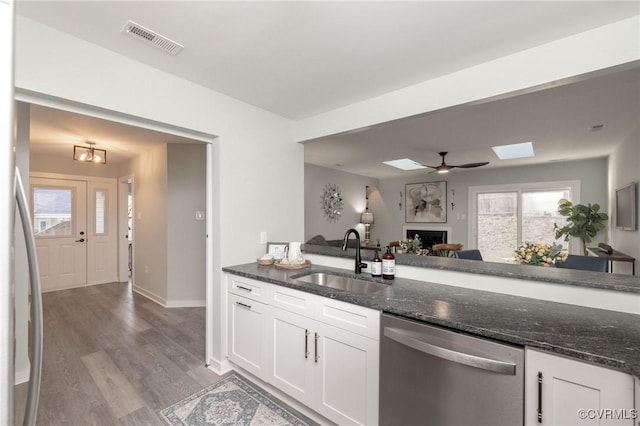 kitchen featuring white cabinetry, light wood-type flooring, dark stone counters, stainless steel dishwasher, and sink