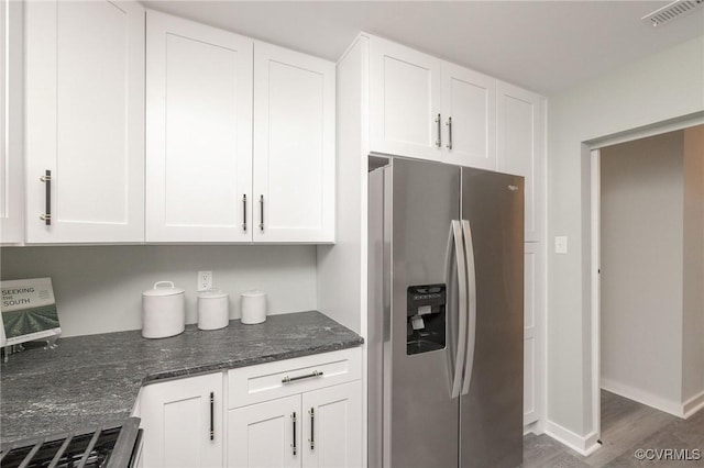 kitchen featuring white cabinetry, stainless steel fridge with ice dispenser, and dark stone counters