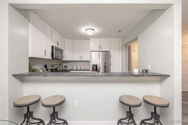 kitchen featuring kitchen peninsula, stainless steel appliances, stone counters, white cabinets, and a breakfast bar