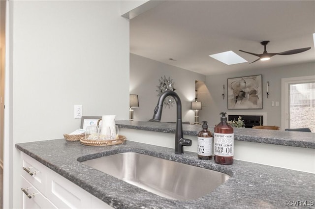 kitchen with ceiling fan, sink, white cabinetry, and a skylight