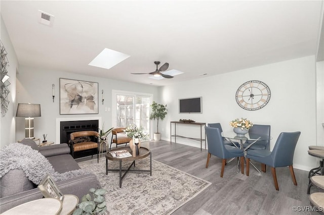 living room featuring ceiling fan, a skylight, and hardwood / wood-style flooring