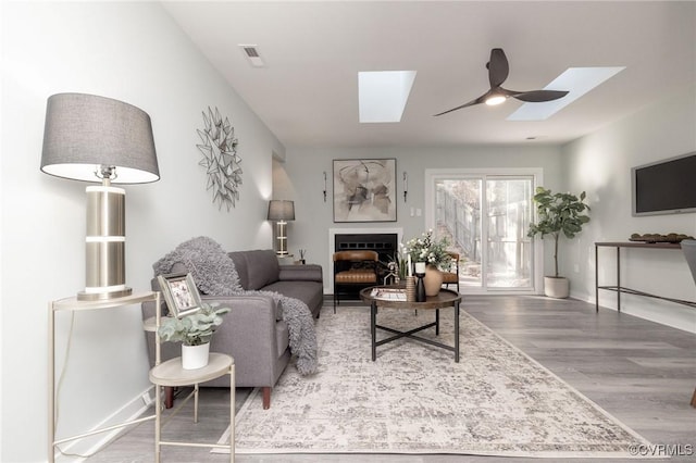 living room featuring ceiling fan, wood-type flooring, and a skylight