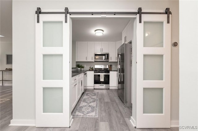 kitchen with white cabinets, appliances with stainless steel finishes, light hardwood / wood-style flooring, and a barn door